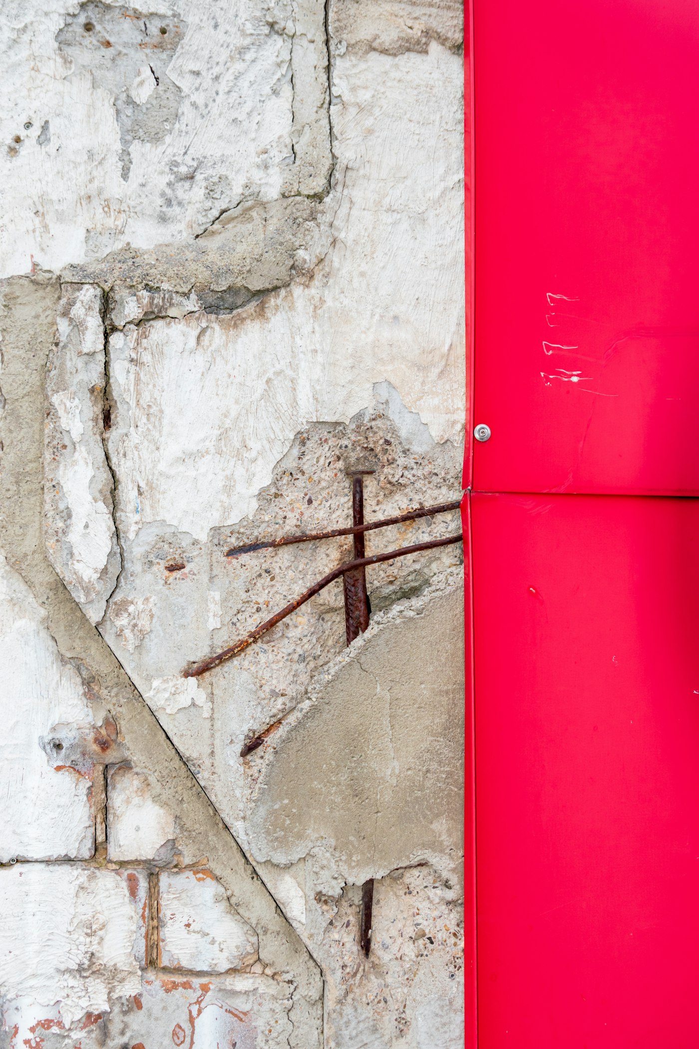 Cracked concrete wall with exposed rusted rebar next to a clean metal panel edge