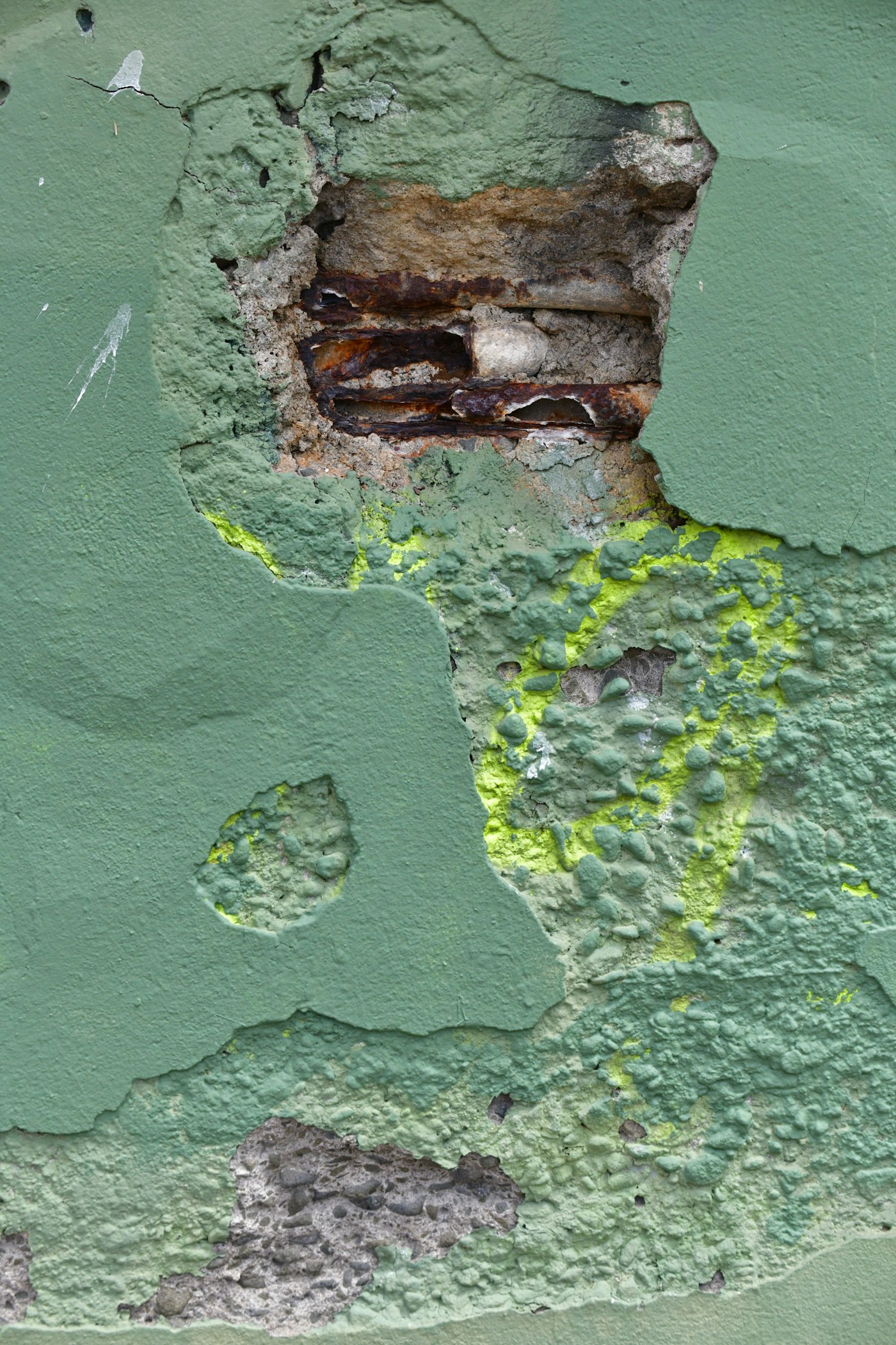 Damaged painted concrete wall with exposed corroded rebar and moisture staining